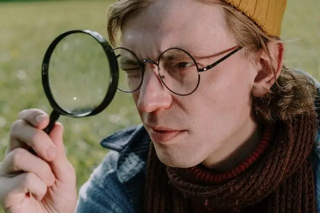 Man in Brown Knitted Scarf Looking at the Magnifying Glass
